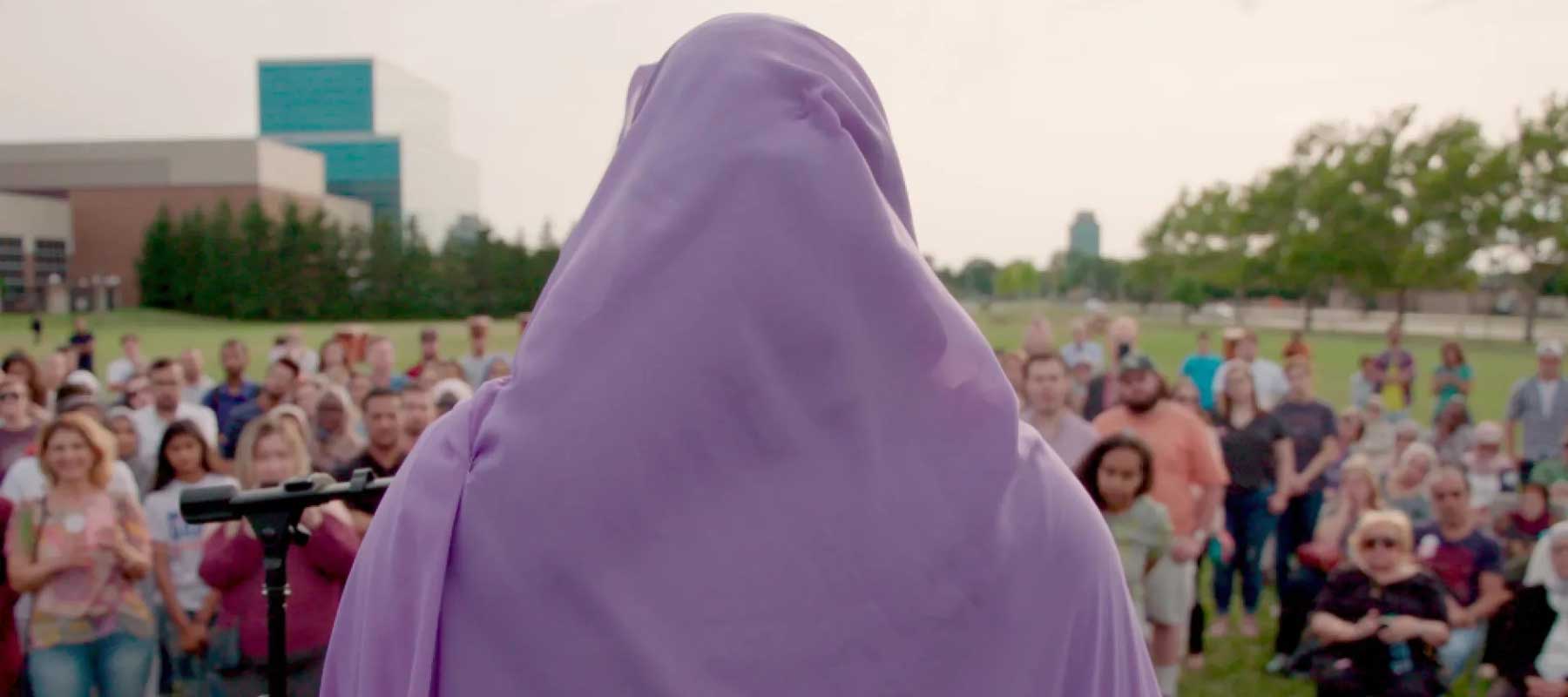 A woman faces towards a crowd and speaks.